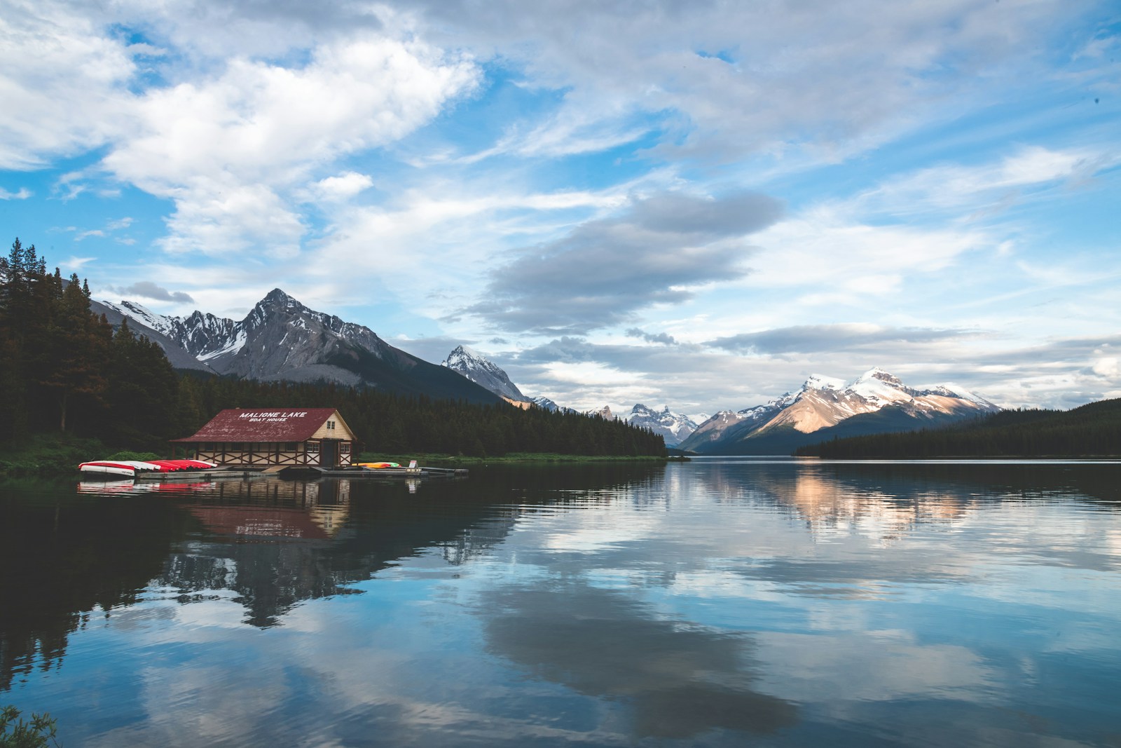 A sunny mountain lake with a boathouse and red canoes